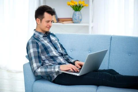 A Young attractive guy man is browsing at his laptop, sitting at home on the  Stock Photos