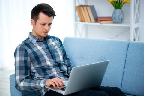A Young attractive guy man is browsing at his laptop, sitting at home on the  Stock Photos