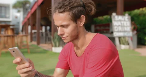 Young attractive guy in a red t-shirt uses a smartphone Stock Footage 107453923
