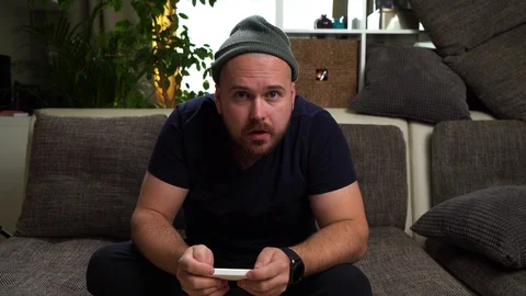 Young attractive guy sitting on the couch and playing console. Win the game and Stock Footage 112722552