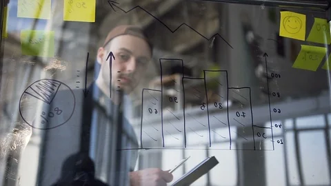 Young attractive hipster man checking diagrams on the glass board. Video stock 108333206