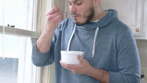 Young attractive hispanic man eats cereal while looking out kitchen window Stock Footage 84474743