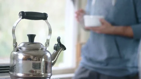 Young attractive hispanic man sets down bowl and pours hot water from tea kettle Stock Footage 84474273