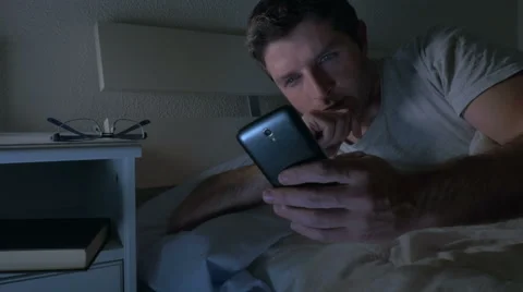 Young attractive man in bed at night networking with Mobile phone Stock Footage 64456393