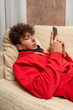 Young attractive man with curly hair dressed in a red sweatshirt using mobile Stock Photos