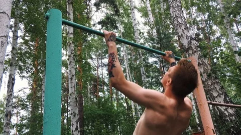 Young attractive man is doing exercise on the parallel bars outdoors. Guy Stock Footage 93819218