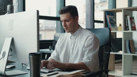 Young attractive man glasses writes in a notebook, looks at the monitor office Stock Footage 81243569