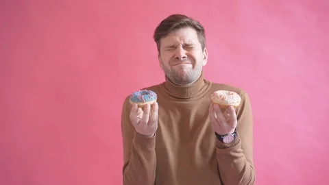 Young attractive man making faces with fresh testy donuts in his hands Stock Footage 123916337