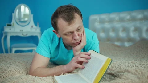 Young attractive man reading a book while lying on the bed Stock Footage 145483376