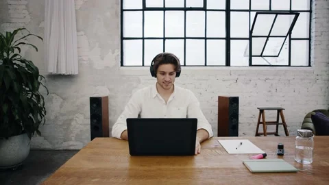 Young attractive man sits in front of his laptop and starts a video call Stock Footage 145734741