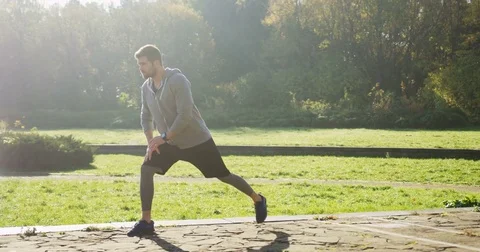Young attractive man stretching his legs early in the morning in the beautiful Stock Footage 82505481