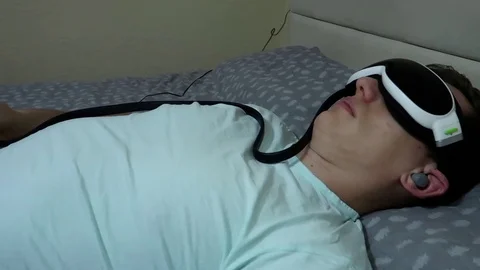 Young attractive man uses an eye massager device, lying on the bed Video stock 104444800