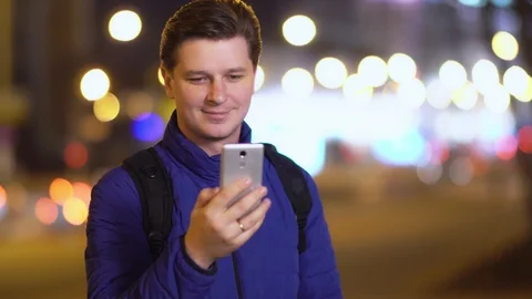 A young attractive man uses a mobile phone in a night city. Video stock 88167919