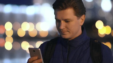A young attractive man uses a mobile phone in a night city. Video stock 88168617