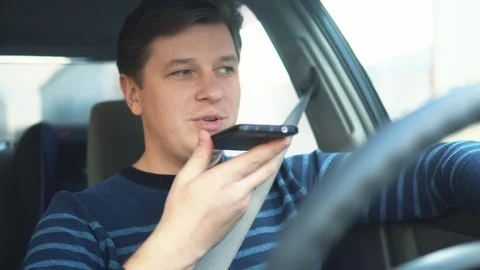 A young attractive man is using a mobile phone on the speakerphone in the car Stock Footage 87350262