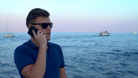 Young attractive man using phone talking via his smartphone on Seafront, calm Stock Footage 118304603