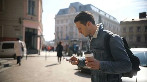 Young attractive man walks down the street holding coffee and using phone Stock Footage 78091960