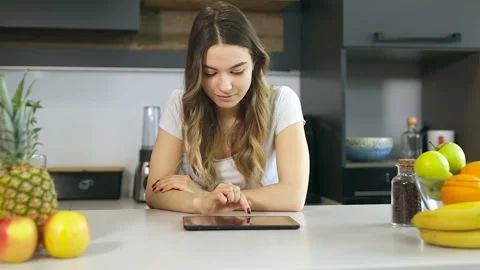 Young, attractive woman using tablet at the kithen. Looking at the camera and sm Stock Footage 104075309