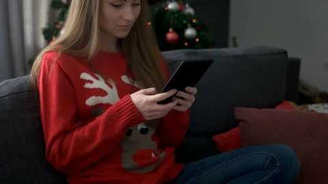 Young attractive woman wearing sweater with deer sitting on sofa and chating Stock Footage