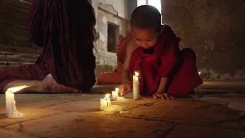 Young authentic real monk boy playing with fire candle in meditation ancient tem Vídeos de archivo 201094327