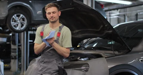 Young auto mechanic standing at open car and repairing motor in big garage. Stock Footage 341864300