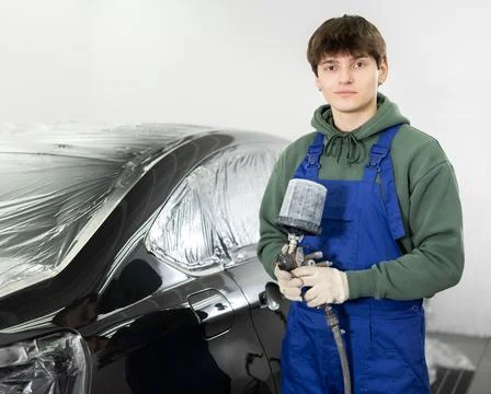 Young auto painter with spray gun standing near car in workshop Stock Photos