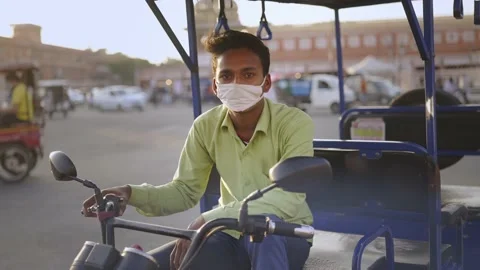 Young auto rickshaw male driver sitting and wearing face mask in a busy market Stock Footage 147011060