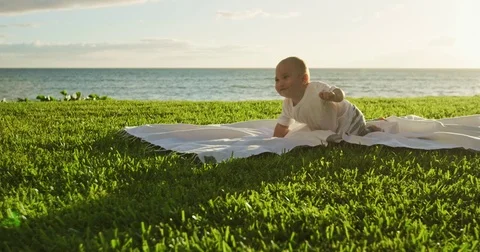 Young baby crawling for the first time on blanket on lawn at sunset Stock Footage 76787093