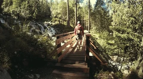 Young backpacker goes to the bridge in alpine forest near the rapid stream Stock Footage 53874230