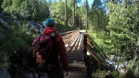 Young backpacker goes to the bridge in alpine forest near the rapid stream Stock Footage 53874244
