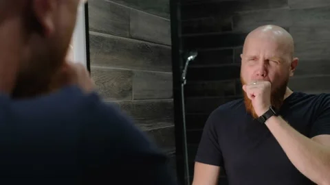A young bald guy with a red beard yawns in front of the bathroom mirror. Stock Footage 138998221