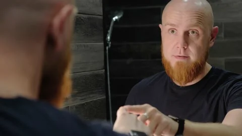 A young, bald guy with a red beard speaks, dances and sings in front of mirror. Video stock 138998464