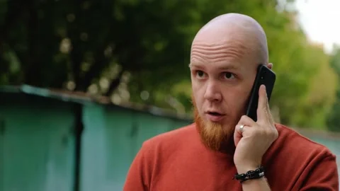 A young bald guy with a red beard on the street speaks seriously on the phone. Stock-Footage 139001613