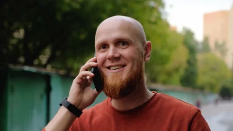 Young bald guy with red beard smiling speaks on the phone on the street Stock Footage 139001923