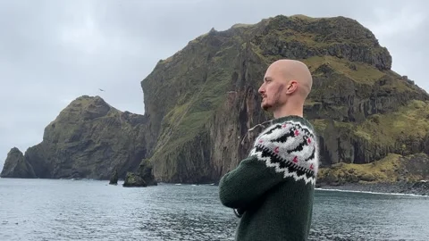A young bald guy stands against the background in an Icelandic sweater Stock Footage 253110059