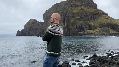 A young bald guy stands against the background in an Icelandic sweater Stock Footage 253110081