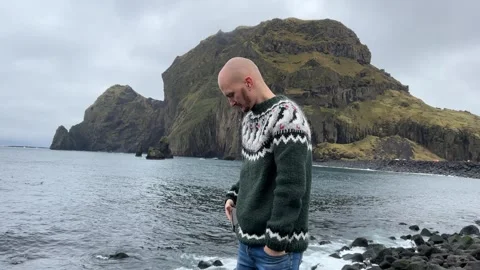 A young bald guy stands against the background in an Icelandic sweater Stock Footage 253402936