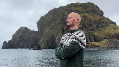 A young bald guy stands against the background in an Icelandic sweater Stock Footage 253402977