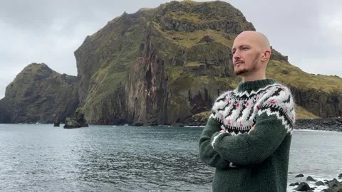 A young bald guy stands against the background in an Icelandic sweater Stock Footage 253403055