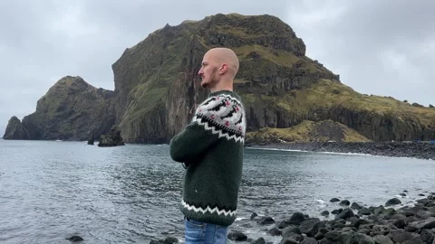 A young bald guy stands against the background in an Icelandic sweater Stock Footage 253403080