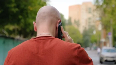 A young bald guy is walking down the street and talking on the phone. Back view. Stock Footage 139001931