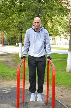Young bald man doing push-ups on parallel bars in a city park Stock Photos
