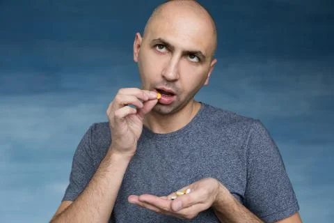 A young bald man eats pills on a blue background. Stock Photos