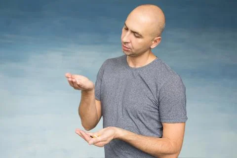 A young bald man eats pills on a blue background. Stock Photos