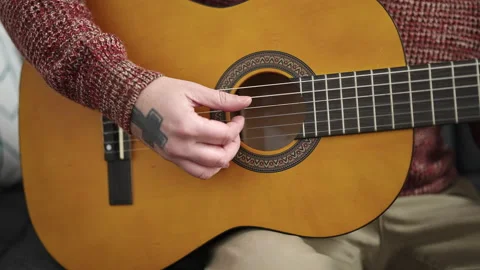 Young bald man playing classical guitar sitting on sofa at home Stock Footage 238586171