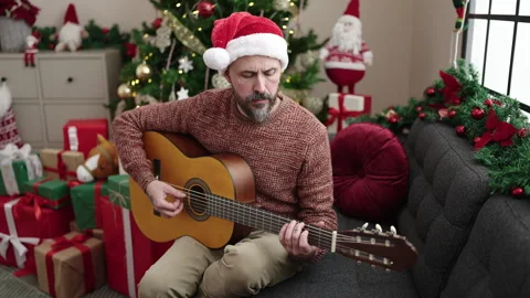 Young bald man playing classical guitar sitting on sofa by christmas tree a.. Stock Footage 249892294