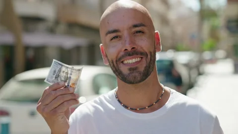 Young bald man smiling confident holding 100 dollars banknote at street Stock Footage 221108883