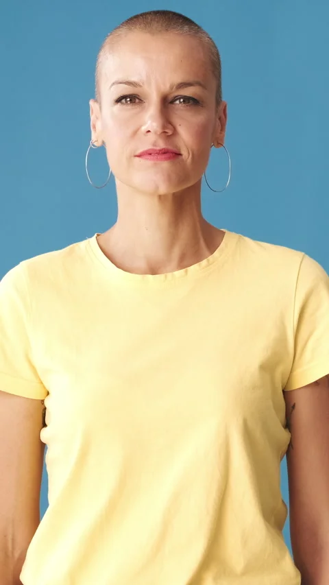 Young bald woman looking at camera on blue background in studio Stock Footage 296113624