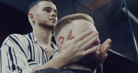 Young barber master arranges a client's beard, massages the skin of the face. Stock Footage 139803492