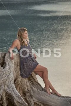 A Young Barefoot Woman in a Slip Relaxing on a Tree Stump Next to a Lake Stock Photos